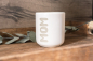 Preview: Matte weiße Keramiktasse mit vertikaler Gravur „MOM“ in moderner Schrift auf Holzuntergrund, Eukalyptus im Hintergrund.
