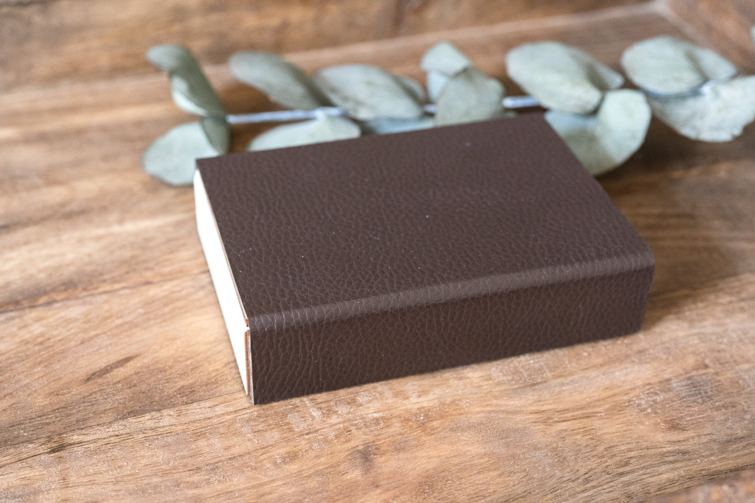 Kleine rechteckige Holzbox für USB‑Stick mit dunkelbraunem Kunstleder‑Umschlag und Magnetverschluss, liegend auf Holztisch – elegante USB‑Geschenkbox