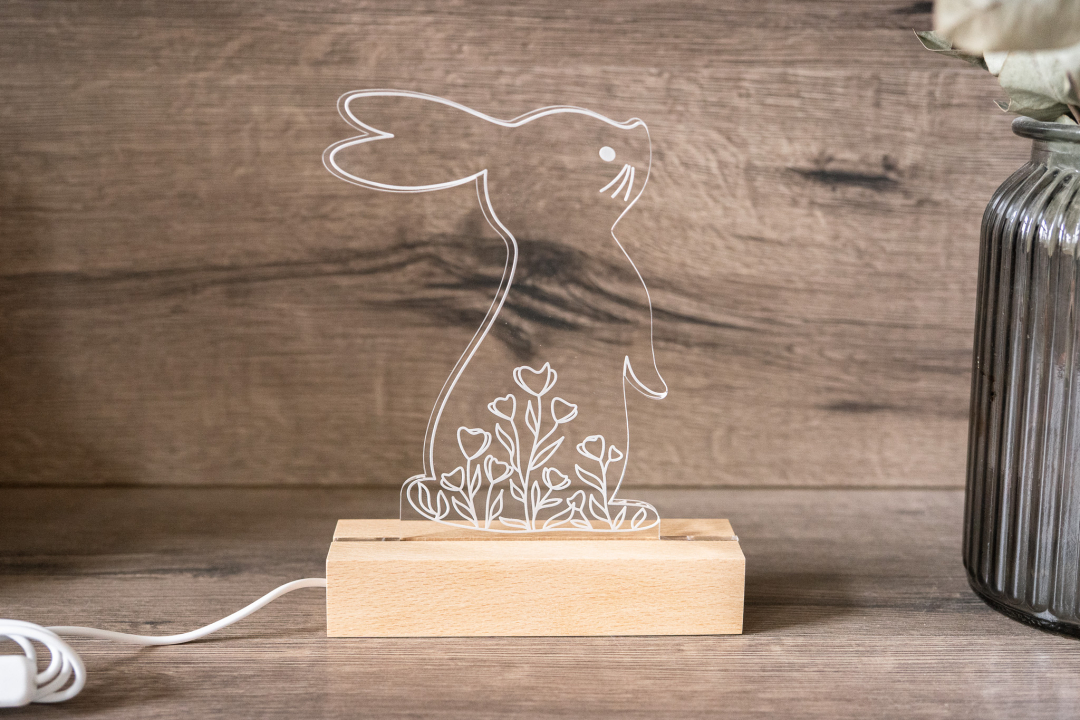 Leuchtende LED Osterlampe mit Hasenmotiv und Blumen aus Acrylglas auf Holzsockel mit warmweißem Licht